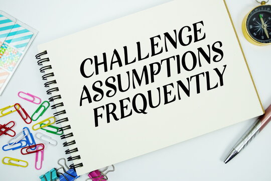 Challenge Assumptions Frequently text message written on notepad with stationery flat lay on white background