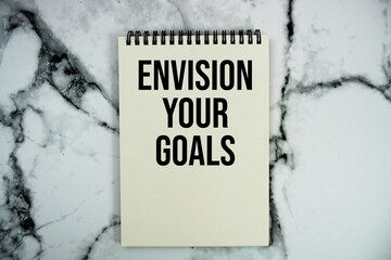 Envision Your Goals text written on notepad flat lay on marble background