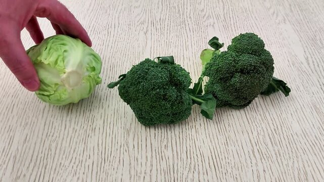 A head of cabbage and two broccoli florets rest on a light wooden surface, arranged in a row to showcase fresh, vibrant produce ideal for healthy cooking or food visuals