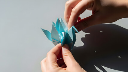 Close-up of hands folding a blue origami flower made from paper in natural light. Creative DIY paper craft concept showing handmade art, creativity, mindfulness, and traditional origami techniques