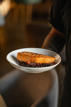 Grilled salmon fillet served by chef on dark background with elegant restaurant presentation