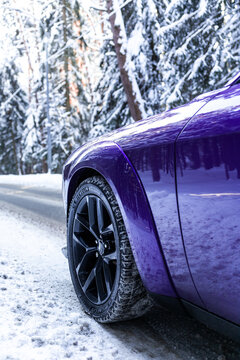 Purple Dodge Challenger SRT muscle car parked in a winter forest landscape. Powerful American sports car with aggressive design, snowy background and dramatic contrast. 