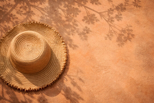 Straw hat on terracotta wall with plant shadows in sunlight. Boho summer vibe with warm tones and nature-inspired composition.