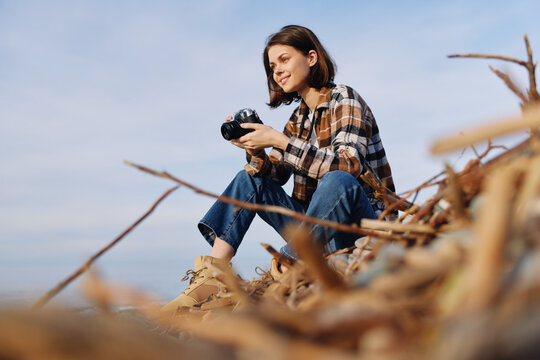 Woman photographer crouches among coastal dunes with a camera, capturing nature, landscape scenes, and bright daylight for an evocative outdoor shot