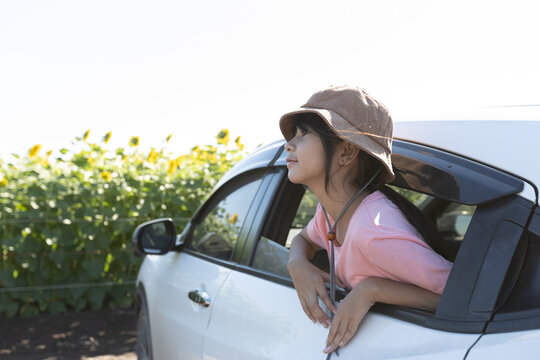Asian girl leaning near a car window while looking outside during a family trip, showing childhood curiosity, travel lifestyle, and relaxed outdoor journey.
