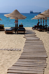 View of a wooden path leading to sun beds and sun umbrellas at the sandy beach of Ios Greece