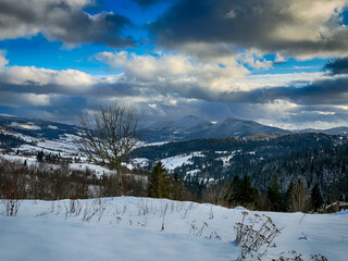 Mystical snowy Carpathian peaks under cloudy skies in the sunny weather