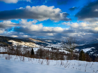 Mystical snowy Carpathian peaks under cloudy skies in the sunny weather
