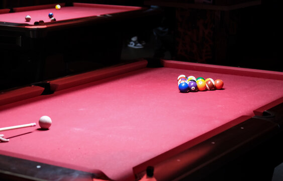 Red pool table with cue stick aimed at cue ball, ready to break a colorful triangle of billiard balls.