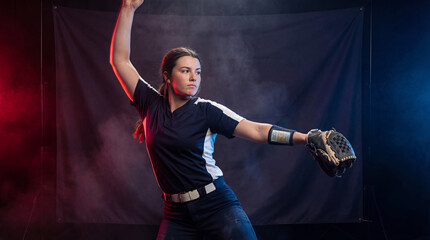 caucasian softball player pitching ball in studio with smoke. female athlete in blue uniform. sport competition concept. banner, website header with copyspace.