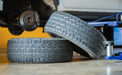 Two car tires with tread pattern stacked on garage floor with vehicle on hydraulic lift and disc brake background in auto repair workshop, Auto service, Mechanic workshop, Puncture repair © Sumala