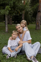 Fototapeta premium A happy mother with two children in a park. The mother, son, and daughter are smiling. The concept of parenting, family