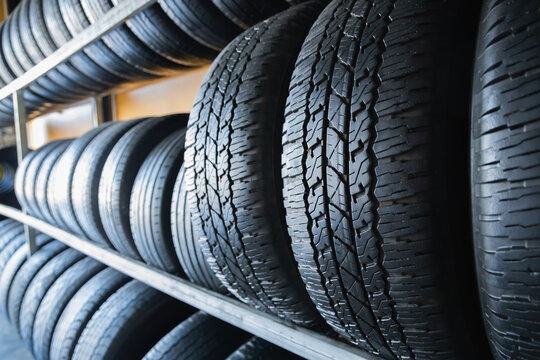 Rows of new black car tires with deep tread pattern stacked on metal rack in auto parts store warehouse inventory, Tire shop, Auto parts store, Inventory Stock Supply Buying tires, Business Commerce