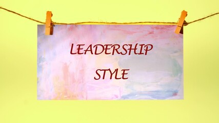 The phrase LEADERSHIP STYLE is slowly revealed on sheets hung by clothespins. The words materialize like a watercolor painting, vivid against the yellow backdrop