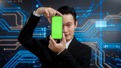 Business Asian man in formal suit executive presents green screen smartphone against blue digital circuit background. fintech innovation, secure cloud computing, digital transformation leadership.
