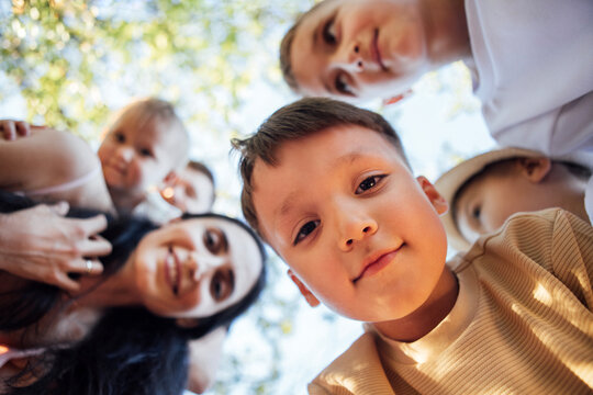 Group of children and adults smiling together outdoors, captured from a low angle, surrounded by greenery, showcasing joy and connection in a vibrant atmosphere