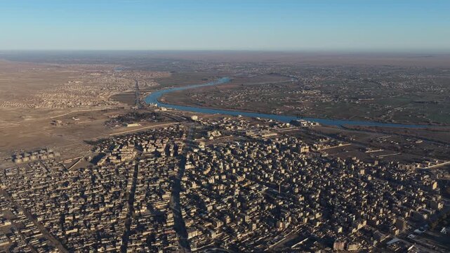 Drone shot overlooking the city of Deir ez-Zor in eastern Syria. The footage captures the urban landscape, traditional architecture, and the strategic flow of the Euphrates River.