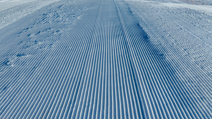 Perfectly groomed ski piste with smooth corduroy snow leading toward alpine slopes, designed for winter sports, resort branding, and seasonal outdoor concepts