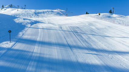 Wide groomed ski slope with smooth corduroy snow surface, prepared for alpine skiing, winter sports, and seasonal resort promotion visuals