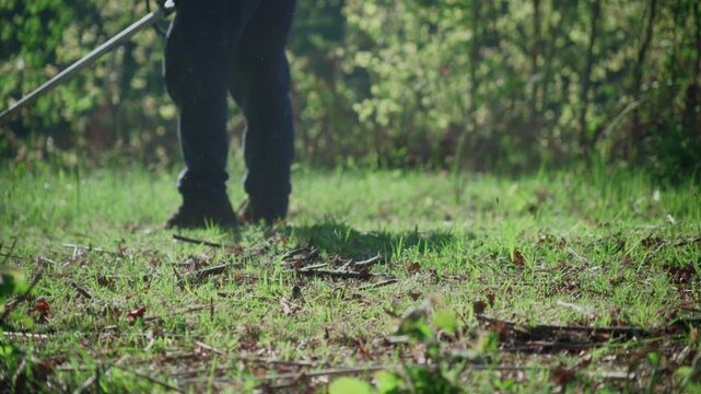 Person trims grass, then lays brush cutter on grassy ground. Ground level view