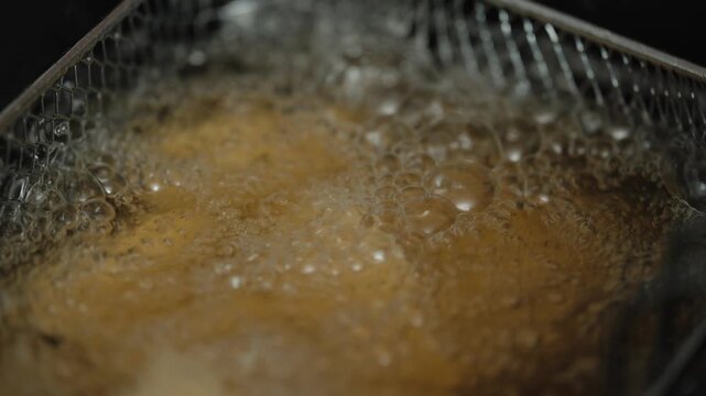 Close up of rissois frying in hot oil inside deep fryer basket