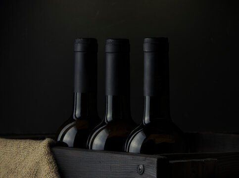 Wine bottles without labels in a wooden box on a dark background