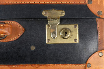 A close-up shot captures the tarnished brass lock mechanism on a vintage black suitcase with contrasting brown leather trim and stitching © nahhan