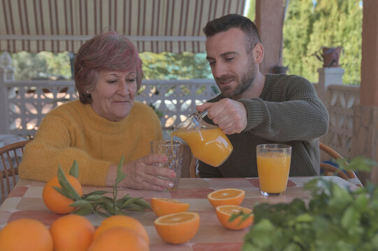 Hijo ech&aacute;ndole zumo de naranja de una jarra a su madre mientras desayunan
