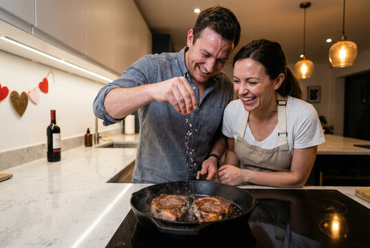 Man and woman cooking steak together in modern kitchen for Valentine's Day  