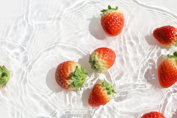Fresh red strawberries floating in clear water with sunlight shadows.