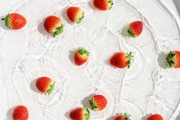 Fresh red strawberries floating in clear water with sunlight shadows.
