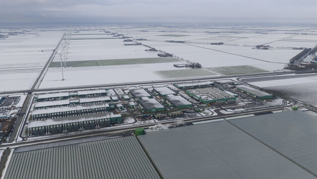 Aerial view of a vast datacenter complex amidst a snow-covered landscape, windmills standing tall in the distance, Datacenter Middenmeer, North Holland, Netherlands.