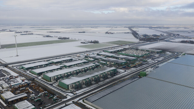 Aerial view of a sprawling datacenter complex nestled amidst snow-dusted fields under a gray sky, a stark contrast of industry and nature, Middenmeer, North Holland, Netherlands.