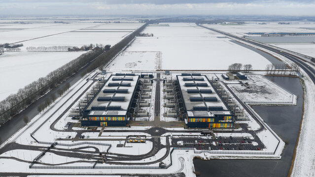 Aerial view of the stark, snow-covered landscape contrasting with the warm glow emanating from the data center, Datacenter Middenmeer, North Holland, Netherlands.