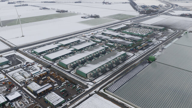Aerial view of snow-dusted greenhouses and industrial buildings create a geometric pattern against the white fields, Agriport Middenmeer, Netherlands.