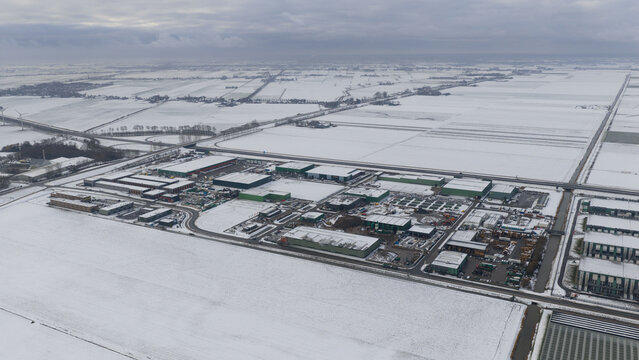 Aerial view of industrial buildings dusted with snow stand in stark contrast against the flat, white landscape under a somber sky, Middenmeer, North Holland, Netherlands.