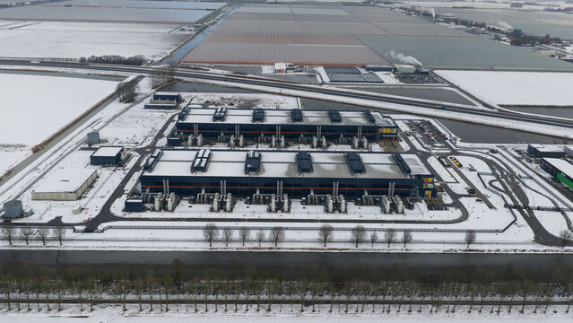 Aerial view of a vast, snow-dusted industrial complex with contrasting dark roofs and bright white surroundings, Middenmeer, North Holland, Netherlands.