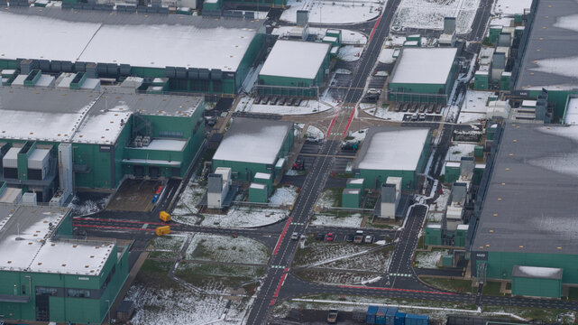 Aerial view of geometric shapes of buildings stand dusted with snow, their green and grey hues contrasting against the crisp white blanket, Agriport Middenmeer, Netherlands.