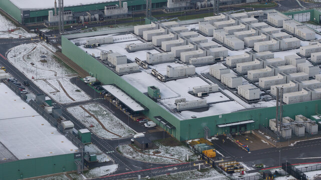 Aerial view of the large, box-like buildings and structures, with light snow cover, creating a stark contrast against the green walls, Datacenter Middenmeer, North Holland, Netherlands.