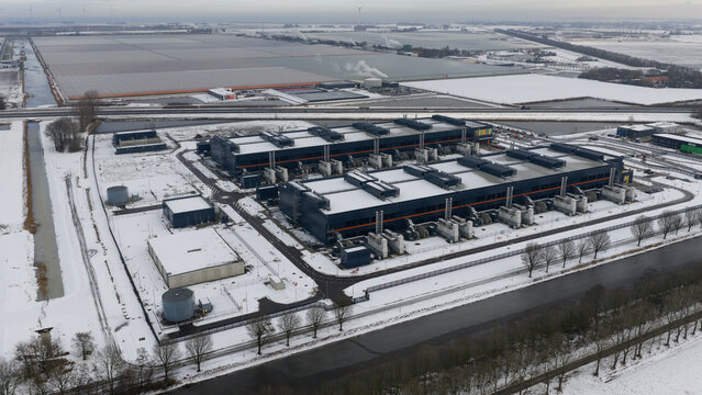 Aerial view of a sprawling datacenter complex surrounded by snow-dusted fields under a pale winter sky, Middenmeer, North Holland, Netherlands.