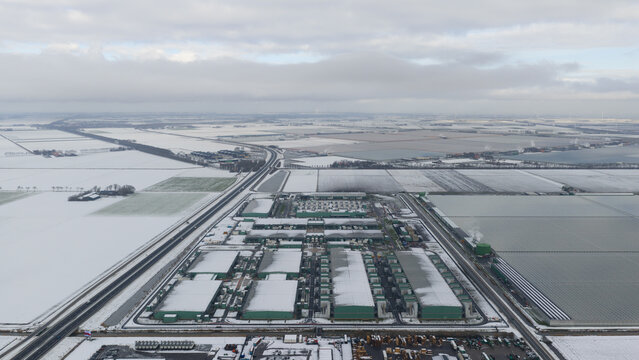 Aerial view of a sprawling data center complex, dusted with snow, stands in stark contrast to the flat, icy landscape, Datacenter Middenmeer, North Holland, Netherlands.