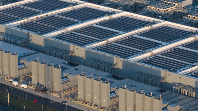 Aerial view of a modern datacenter complex with rows of solar panels casting shadows in the late afternoon sun, Winschoten, Groningen, Netherlands.