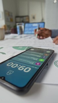 Vertical closeup of smartphone displaying notifications while lying on workplace desk covered with paper documents and unrecognizable employee working in office environment