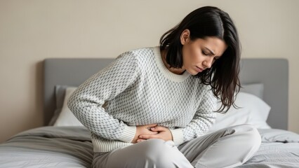 Obraz premium Young woman in bed suffering from severe stomach pain feeling discomfort possibly due to cramps or illness