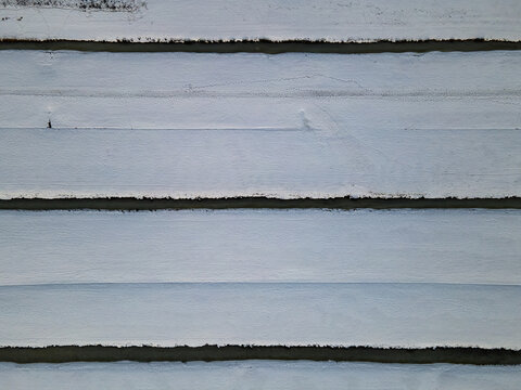 Aerial view of snow-covered fields divided by dark canals creates a stark, geometric landscape, Delft, South Holland, Netherlands.