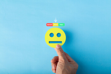 Hand holding a yellow neutral face emoticon with a mood scale pointing to the average level. Conceptual image for indifferent feedback, mental health screening, and customer experience assessment.