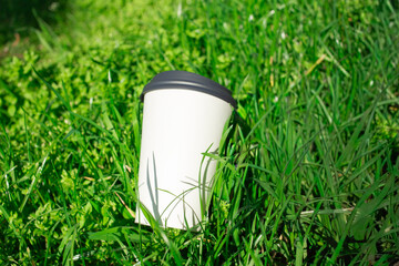 Discarded paper cup lying on green grass as  pollution concept