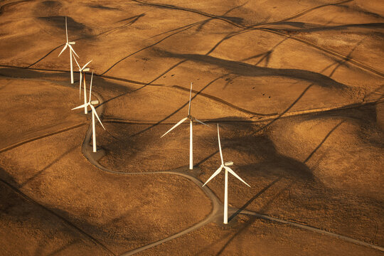 Aerial view of wind turbines casting long shadows across the golden, undulating hills, Altamont Pass, California, United States.