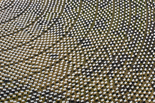 Aerial view of a solar thermal power plant's vast field of heliostats reflecting sunlight, Seville, Andalusia, Spain.