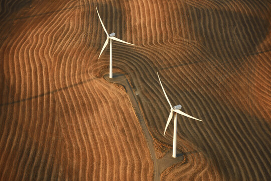 Aerial view of two wind turbines casting long shadows over the rippled, golden fields, creating a striking contrast of light and shadow, Washtucna, Washington, United States.